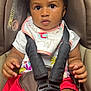 baby, child, car_seat, seatbelt, bib, clothing, red_shorts, face, hands, infant, sitting, straps, safety, cute, young, portrait, indoor, person, expression, attention