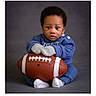 Jeremiah joined the competition — help win amazing prizes! baby, blue_clothing, child, cozy, cute, expression, feet, football, hands, indoor, infant, knitwear, mittens, portrait, serious, sitting, soft_lighting, sports_equipment, studio, young_child