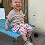 toddler, child, smiling, sitting, outdoor, clothing, shoes, chair, wooden_door, wall, happy, person, face, footwear, pavement, casual_wear, baby, joy, cute, playful