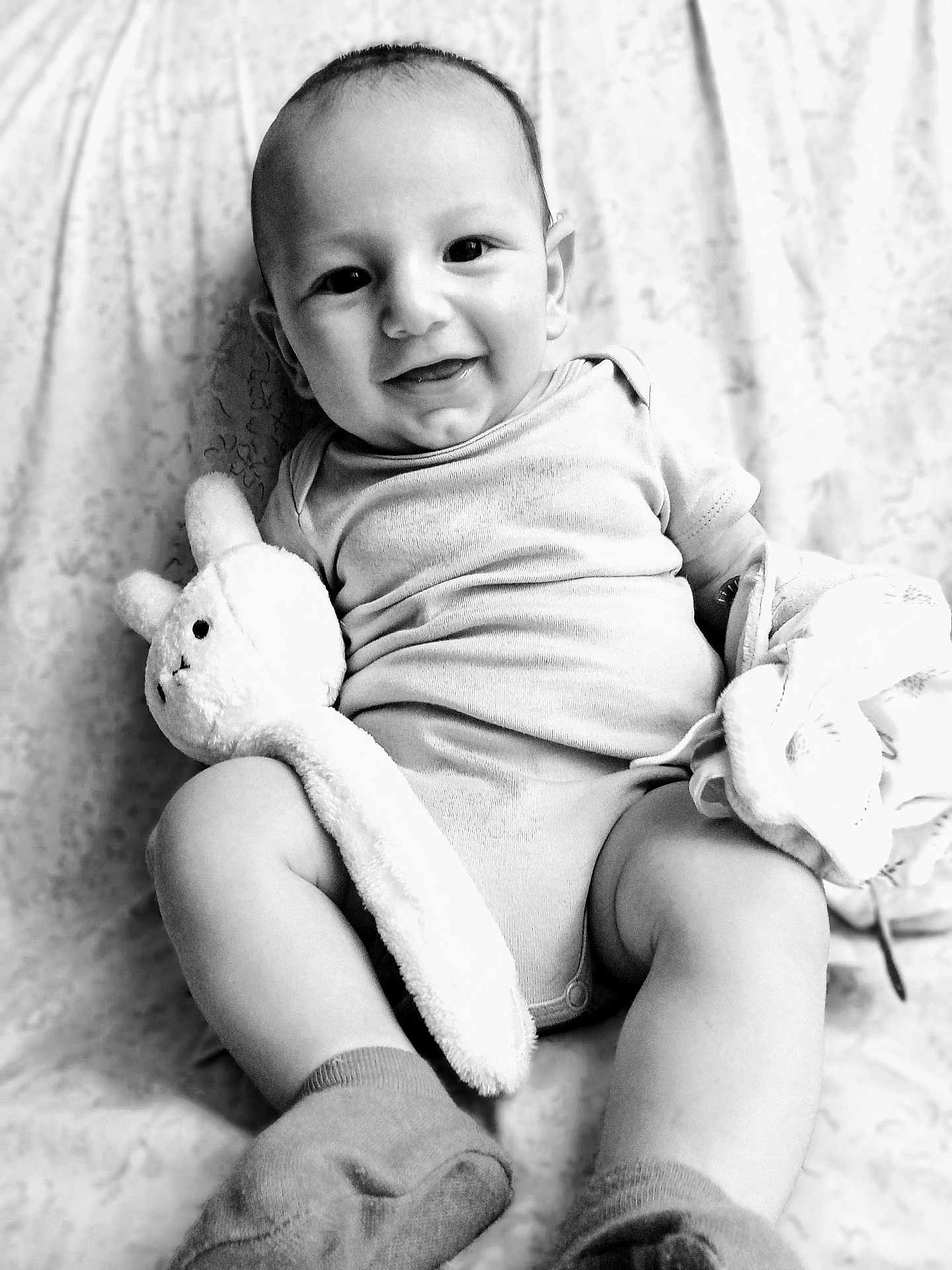 Bennett a rejoint le concours — aidez-le/la à gagner de superbes lots ! baby, smile, onesie, plush_toy, blanket, socks, infant, face, happy, cute, child, portrait, black_and_white, soft_toy, sitting, fabric, cozy, indoor, young_child, cuddly