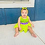 baby, child, green_dress, headband, sitting, concrete_floor, blue_wall, window, curious_expression, barefoot, outdoor, portrait, infant, person, smiling, purple_flowers, summer, cute, young_child, casual