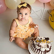 Maddie joined the competition — help win amazing prizes! baby, toddler, cake, birthday, balloons, yellow_dress, headband, smudged_face, cream, chocolate, celebration, party, sitting, happy, messy, food, cute, indoor, child, portrait