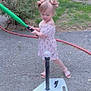 toddler, child, baseball, bat, baseball_tee, backyard, grass, pavement, green_bat, pink_dress, hair_bows, summer, play, outdoor, sport, toy, fence, plants, sandals, concrete