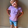child, girl, smiling, standing, purple_tshirt, butterfly, denim_shorts, rainbow_shoes, socks, light_skin, short_hair, earrings, wooden_floor, wall, indoor, casual_clothing, happy, pose, playful, portrait