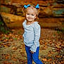 child, girl, blue_bows, pigtails, white_top, blue_jeans, black_boots, forest, leaves, autumn, outdoor, smiling, standing, nature, portrait, cute, young, person, fall, casual_wear