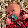 baby, newborn, pacifier, red_shirt, plaid, face, hand, christmas_ornaments, gold, blanket, fluffy, holiday, cute, infant, close_up, indoor, decorations, soft_texture, portrait, child