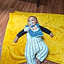 Noham a rejoint le concours — aidez-le/la à gagner de superbes lots ! baby, child, pacifier, bib, plush_toy, yellow_blanket, striped_pants, wooden_floor, smiling, lying_down, indoor, cute, happy, infant, clothing, footwearless, face, head, person, comfort