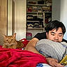 cat, person, bed, blanket, phone, pillow, indoor, furniture, clothing, room, relaxing, orange_cat, casual, technology, portrait, resting, home, sleepwear, cute, companion