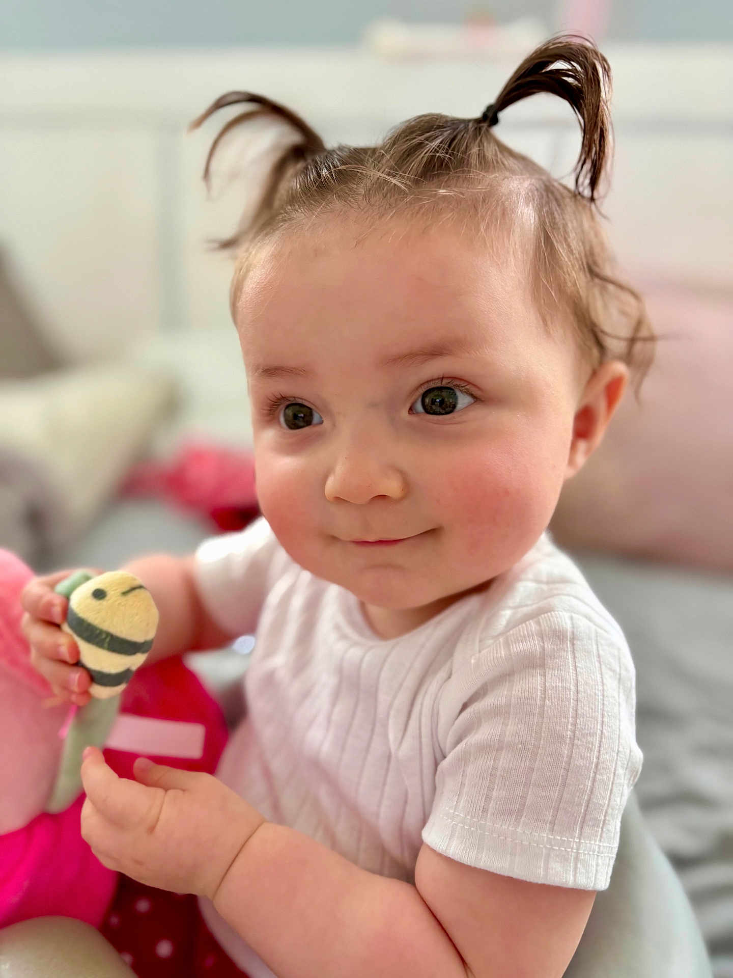 Lucy is registered to the contest to win money with this photo: baby, child, face, pigtails, toy, white_shirt, smile, indoor, cute, skin, hand, person, infant, closeup, expression, soft_light, cheeks, curly_hair, happy, playing