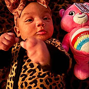 Journi is registered to the contest to win money with this photo: baby, infant, leopard_print, bow, headband, pink, plush_toy, care_bear, stuffed_animal, blanket, pattern, cute, child, portrait, lying_down, soft_toys, animal_print, smiling, indoor, cozy