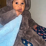 Mesziah is registered to the contest to win money with this photo: toddler, child, baby, blanket, clothing, hat, fuzzy, sitting, indoors, hand, face, eyes, fingers, blue_blanket, brown_outfit, curious, cute, warm, cozy, floral_pattern