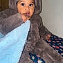 toddler, child, baby, blanket, clothing, hat, fuzzy, sitting, indoors, hand, face, eyes, fingers, blue_blanket, brown_outfit, curious, cute, warm, cozy, floral_pattern