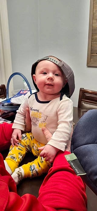 Karson is registered to the contest to win money with this photo: baby, baby_products, baby_toddler_clothing, cap, chair, cheek, child, comfort, fun, happy, headwear, human_leg, lap, person, personal_protective_equipment, picture_frame, room, sitting, skin, t_shirt