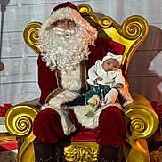 Cassie is registered to the contest to win money with this photo: santa_claus, baby, infant, beard, red_suit, golden_throne, holiday, christmas, festive, portrait, costume, chair, indoor, headband, smile, decor, gift_boxes, fur_trim, boots, people