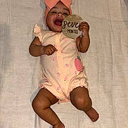 Cassie is registered to the contest to win money with this photo: baby, infant, smiling, headband, bow, onesie, milestone_sign, seven_months, wooden_sign, lying_down, blanket, cute, happy, dark_skin, arm, leg, bare_feet, portrait, indoor, celebration