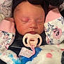 baby, newborn, sleeping, pacifier, headband, black_bow, blanket, car_seat, floral_pattern, pink, clothing, infant, face, peaceful, cute, cozy, child, indoors, closeup, baby_accessory