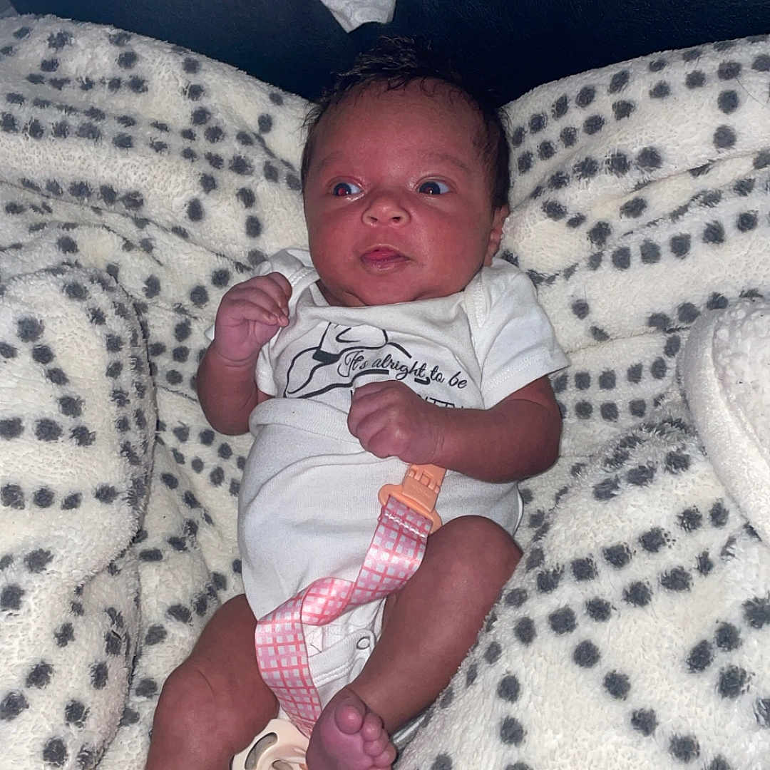 Rayellie-Marie is registered to the contest to win money with this photo: baby, blanket, clothing, comfort, cute, expression, face, foot, hand, indoor, infant, lying_down, newborn, onesie, pacifier, patterned_blanket, person, skin, soft, toddler