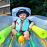 Karter is registered to the contest to win money with this photo: toddler, child, inflatable_pool, life_vest, bucket_hat, pool_noodle, outdoor, summer, water_toys, green_ball, yellow_ball, happy, smiling, play, sunny, nature, fence, relaxing, colorful, fun