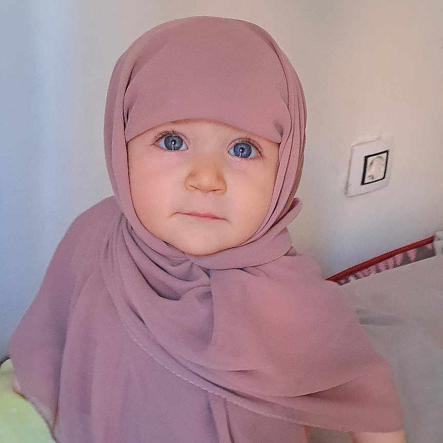 Alaa participe au concours pour gagner de l'argent avec cette photo : baby, bed, blanket, blue_eyes, child, clothing, cozy, curious, cute, expression, face, head_covering, hijab, human, indoors, person, portrait, soft_lighting, toddler, young_child