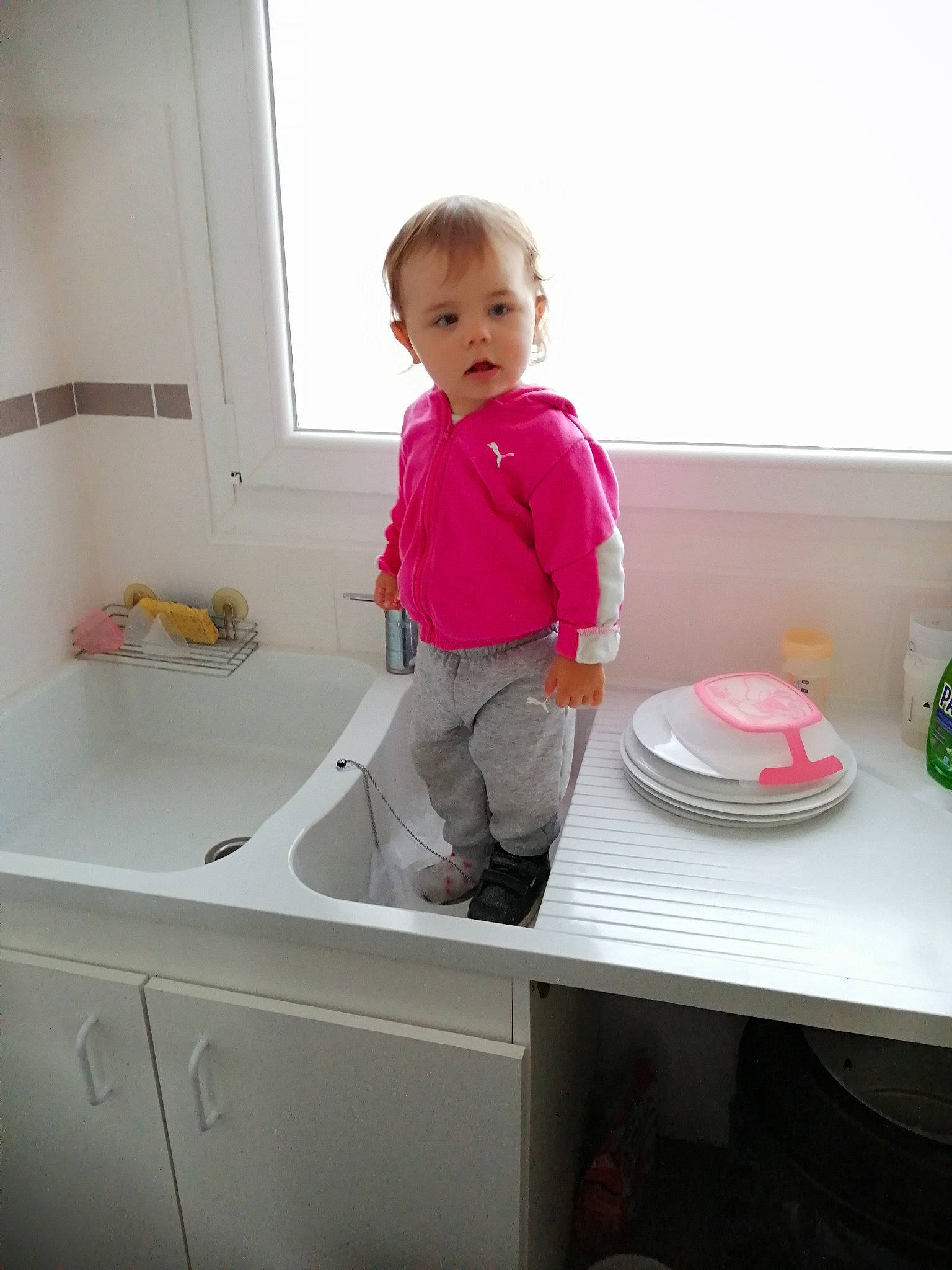 Lily participe au concours pour gagner de l'argent avec cette photo : cabinetry, child, dishware, floor, flooring, home_appliance, kitchen, kitchen_sink, magenta, material_property, person, pink, plumbing_fixture, room, sink, sleeve, table, tableware, tap, toddler