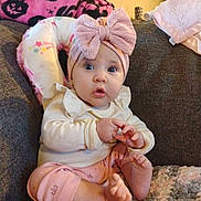 Alyana is registered to the contest to win money with this photo: baby, child, infant, pink_bow, headband, couch, blanket, clothing, sitting, indoor, cute, expression, hands, feet, person, portrait, soft_toys, cozy, curious, home