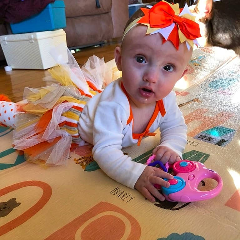 Everly is registered to the contest to win money with this photo: baby, baby_playing_with_toys, baby_toddler_clothing, carmine, child, event, flooring, fun, happy, headwear, holiday, learning, orange, person, play, room, sitting, stuffed_toy, surprise, textile