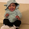 Ilayda a rejoint le concours — aidez-le/la à gagner de superbes lots ! adorable, baby, black_leggings, couch, ears_on_hood, eyes, face, footwear, hands, hooded_jacket, indoor, infant, joyful, playful, portrait, sitting, smiling, tongue_out, white_shoes, zipper