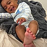 Ilayda participe au concours pour gagner de l'argent avec cette photo : baby, bed, bedding, blanket, child, cozy, curly_hair, dark_hair, earring, feet, foot, happy, indoor, infant, laughing, lying_down, onesie, portrait, smiling, striped_onesie