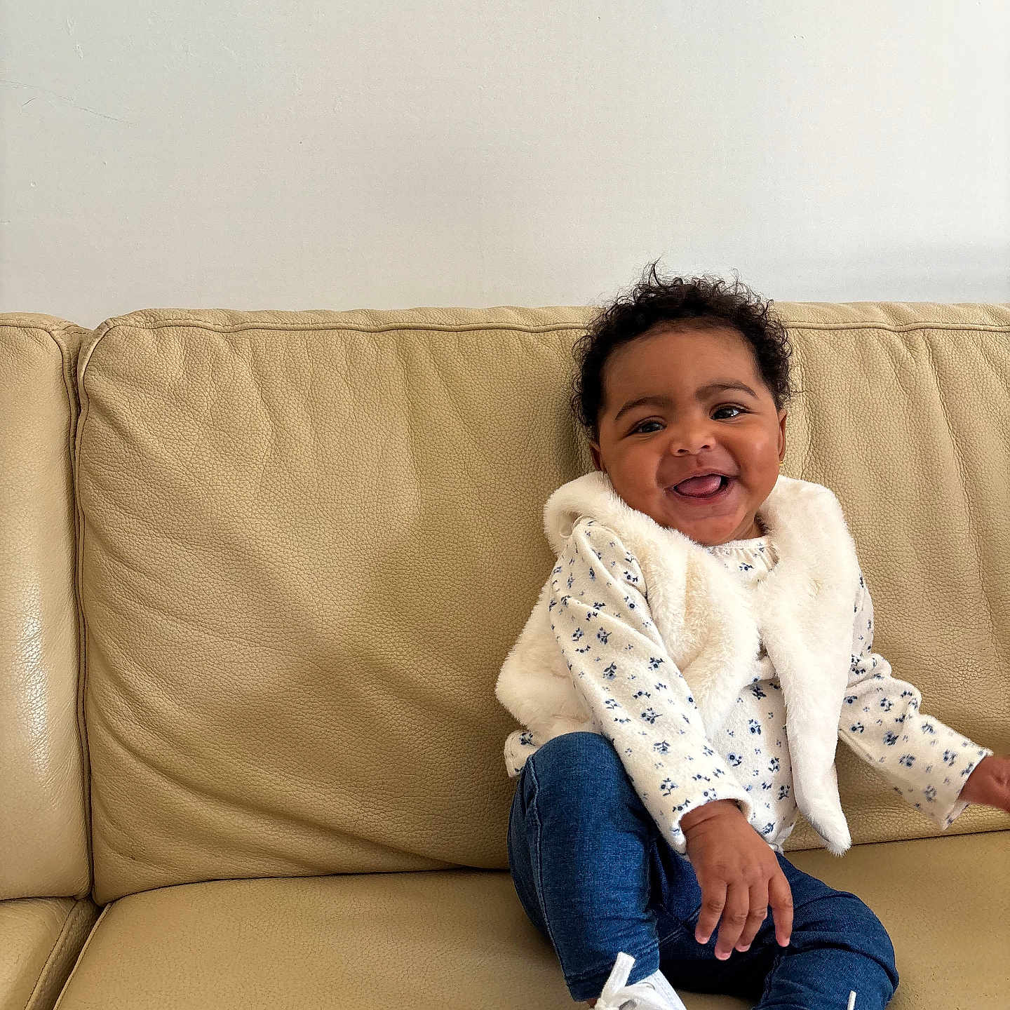 Ilayda participe au concours pour gagner de l'argent avec cette photo : baby, beige, child, clothing, couch, curly_hair, fur_vest, happy, indoor, infant, jeans, living_room, portrait, seated, skin, smile, sneakers, sofa, tiny_shoes, toyless