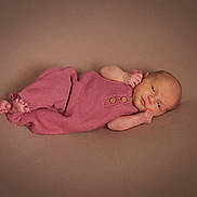 Dakota is registered to the contest to win money with this photo: newborn, baby, infant, child, portrait, lying_down, pink_outfit, knitted_clothing, baby_bodysuit, bare_feet, hands, face, eyes_open, studio, soft_lighting, warm_tones, blanket, cozy, adorable, photography