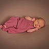 newborn, baby, infant, child, portrait, lying_down, pink_outfit, knitted_clothing, baby_bodysuit, bare_feet, hands, face, eyes_open, studio, soft_lighting, warm_tones, blanket, cozy, adorable, photography
