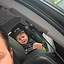 child, toddler, car_seat, car_interior, seatbelt, person, shoe, window, suburban, road, daylight, smile, happy, casual_clothing, head, hair, car_door, seat, adult, portrait
