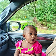 Arden joined the competition — help win amazing prizes! toddler, child, car_interior, pink_dress, green_bows, person, hand, window, side_view_mirror, trees, road_sign, seat, curious, expression, earrings, adult_hand, vehicle, casual, daylight, portrait