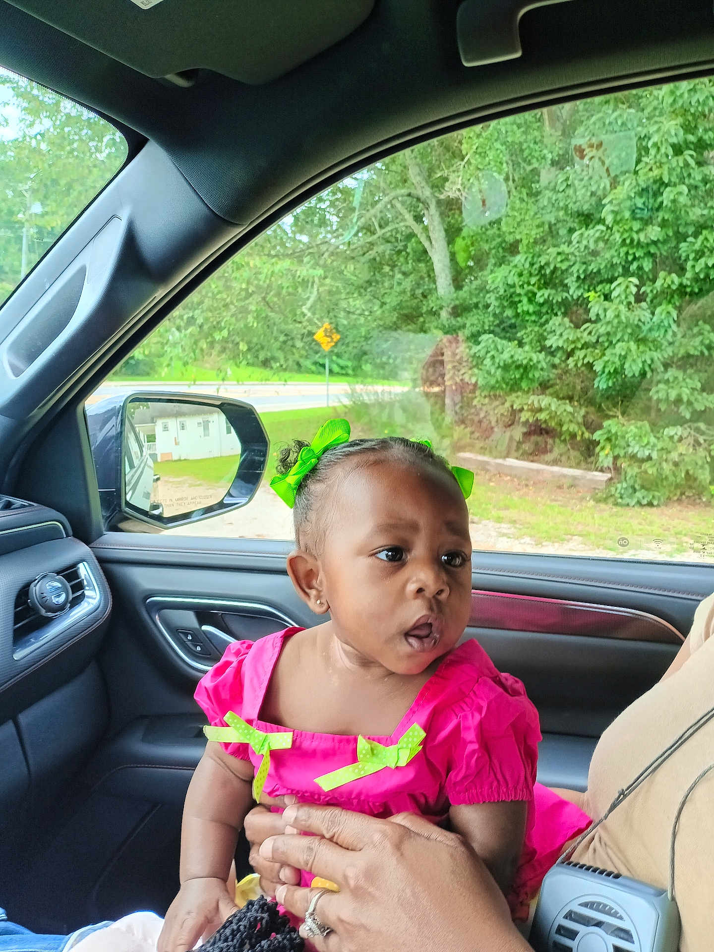 Arden joined the competition — help win amazing prizes! toddler, child, car_interior, pink_dress, green_bows, person, hand, window, side_view_mirror, trees, road_sign, seat, curious, expression, earrings, adult_hand, vehicle, casual, daylight, portrait