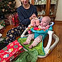 Elizabeth is registered to the contest to win money with this photo: baby, child, woman, christmas_tree, presents, gift_wrap, floor, wood_floor, baby_seat, toys, holiday, decorations, cabinet, figurines, sitting, indoor, clothing, smile, happy, family