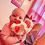baby, child, stuffed_toy, plush, pink_clothing, heart_pattern, indoor, curtains, wall_art, person, holding, cute, infant, soft_toy, face, legs, colorful, cozy, light, gaze