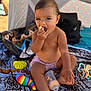 toddler, child, baby, eating, snack, bottle, toys, colorful, blanket, patterned, outdoor, sun_tent, shade, summer, bare_chest, sitting, curious, mischievous, hand, foot