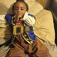 Sion is registered to the contest to win money with this photo: toddler, child, pirate_costume, blue_jacket, brown_pants, bed, pillows, hand, face, curious, indoor, young_child, sitting, costume, clothing, person, cute, portrait, resting, infant