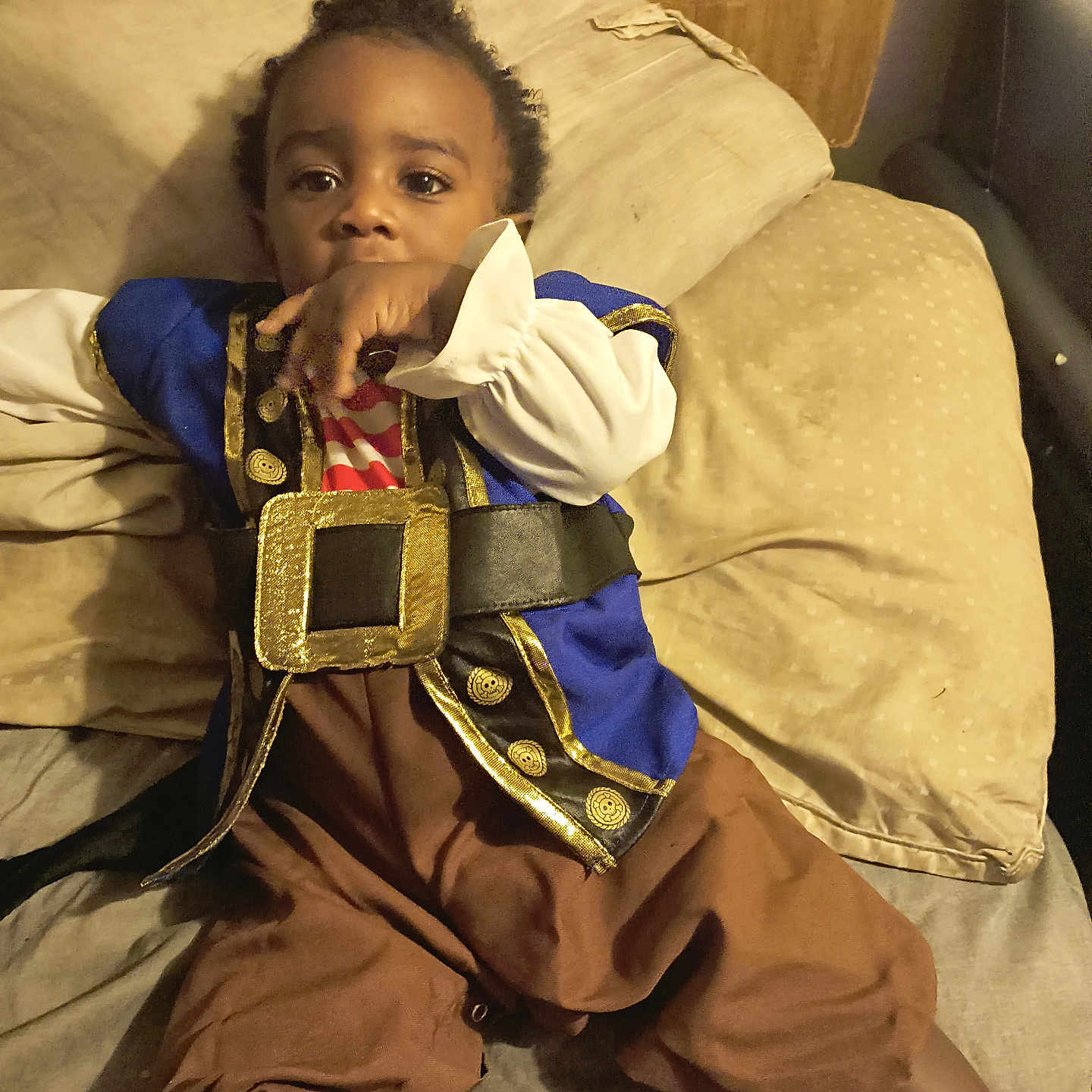 Sion is registered to the contest to win money with this photo: bed, blue_jacket, brown_pants, child, clothing, costume, curious, cute, face, hand, indoor, infant, person, pillows, pirate_costume, portrait, resting, sitting, toddler, young_child