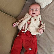Noam a rejoint le concours — aidez-le/la à gagner de superbes lots ! baby, infant, smiling, red_pants, striped_shirt, vest, couch, cushion, happy, face, person, child, lying_down, cozy, soft_texture, indoor, cute, clothing, small_hand, bright_eyes