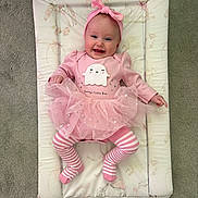 Isla is registered to the contest to win money with this photo: baby, pink, tutu, striped_leggings, headband, smile, face, infant, cute, lying_down, carpet, changing_pad, clothing, happy, child, person, indoors, soft_toys_pattern, playful, adorable