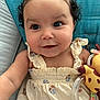 baby, child, curly_hair, dress, toy, giraffe, smiling, face, arm, cushion, blue, seat, indoor, portrait, closeup, happy, infant, person, cute, clothing