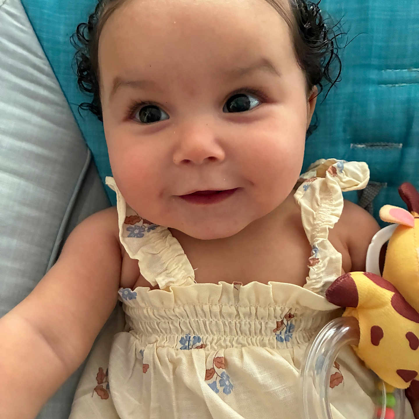 Anivia is registered to the contest to win money with this photo: arm, baby, blue, child, closeup, clothing, curly_hair, cushion, cute, dress, face, giraffe, happy, indoor, infant, person, portrait, seat, smiling, toy