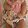 baby, infant, smiling, headband, curly_hair, pink_clothing, floral_pattern, blanket, lying_down, skin, hand, foot, cute, child, person, indoors, soft_toys, adorable, happy, portrait