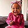 baby, child, infant, smiling, happy, portrait, pink_outfit, headband, bow, seated, bed, indoors, bedroom, closeup, face, curly_joy, dark_skin, fashion, playful, photography