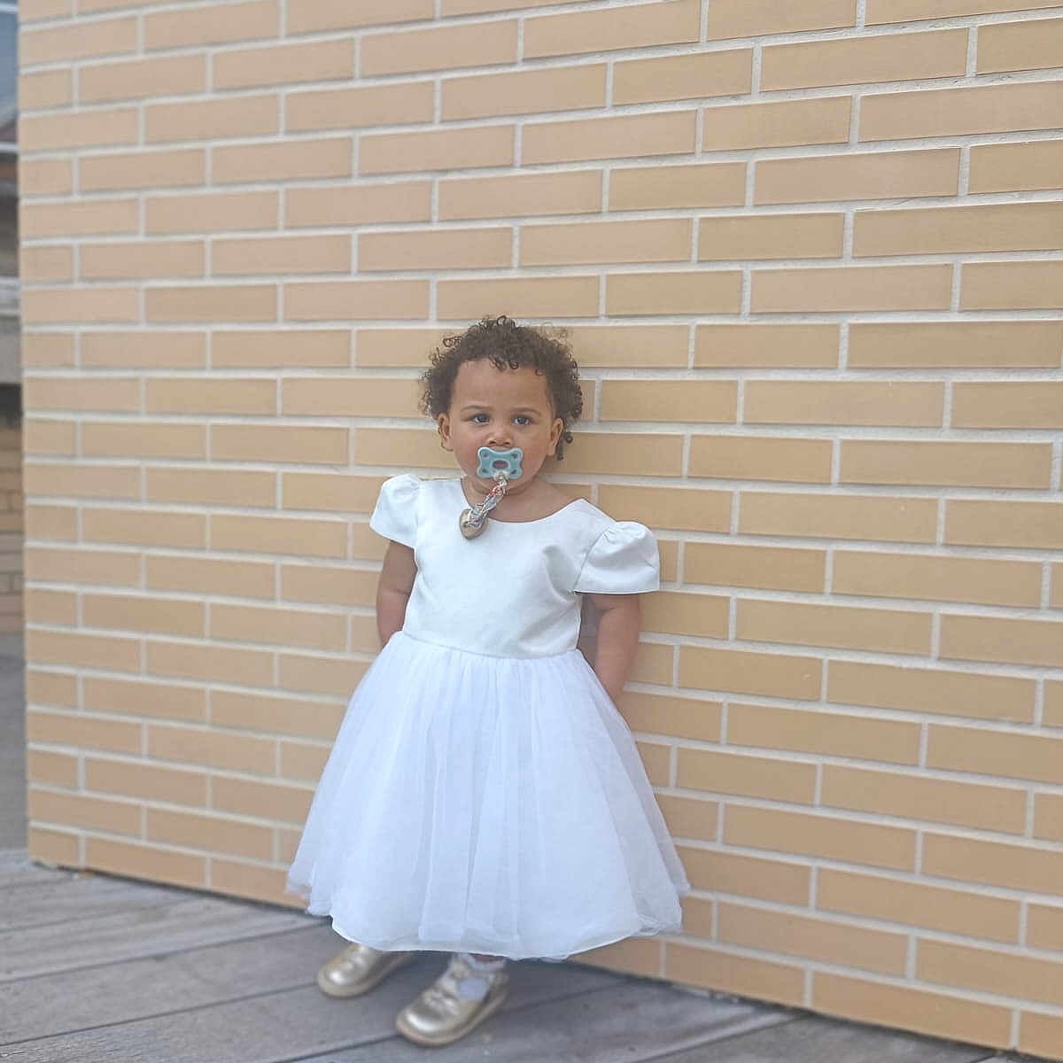 Leila a rejoint le concours — aidez-le/la à gagner de superbes lots ! architecture, brick, building, child, clothing, dress, face, female, formalwear, girl, hair, head, pants, person, photography, portrait, sitting, sleeve, standing, wall