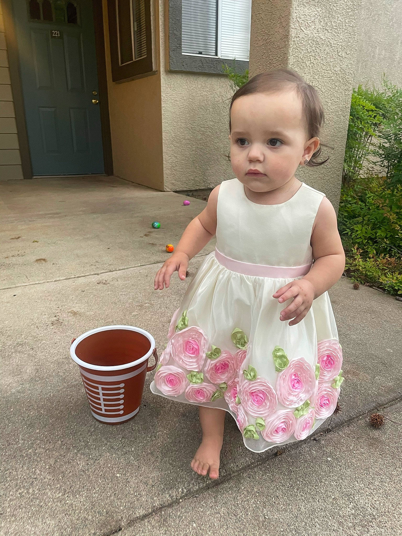 Nyomi is registered to the contest to win money with this photo: baby, baby_toddler_clothing, bucket, cabinetry, child, day_dress, door, dress, flooring, fun, magenta, pattern, person, pink, plant, play, sitting, standing, toddler, vacation