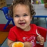toddler, child, smiling, curly_hair, red_shirt, spoon, yellow_cup, table, indoor, daycare, children, happy, playroom, blue_chair, food, snack, person, portrait, cute, seated