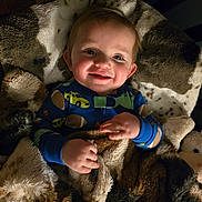 Chance is registered to the contest to win money with this photo: baby, child, smiling, blanket, pajamas, cozy, indoor, cute, happy, face, hands, soft, warm, car_print, football_print, infant, portrait, comfortable, bedroom, toddler