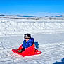 Chance is registered to the contest to win money with this photo: child, toddler, sled, snow, winter, mountains, blue_sky, jacket, hat, sunglasses, outdoor, cold, snowy_field, sunny, shadow, play, recreation, fun, winter_clothing, daytime